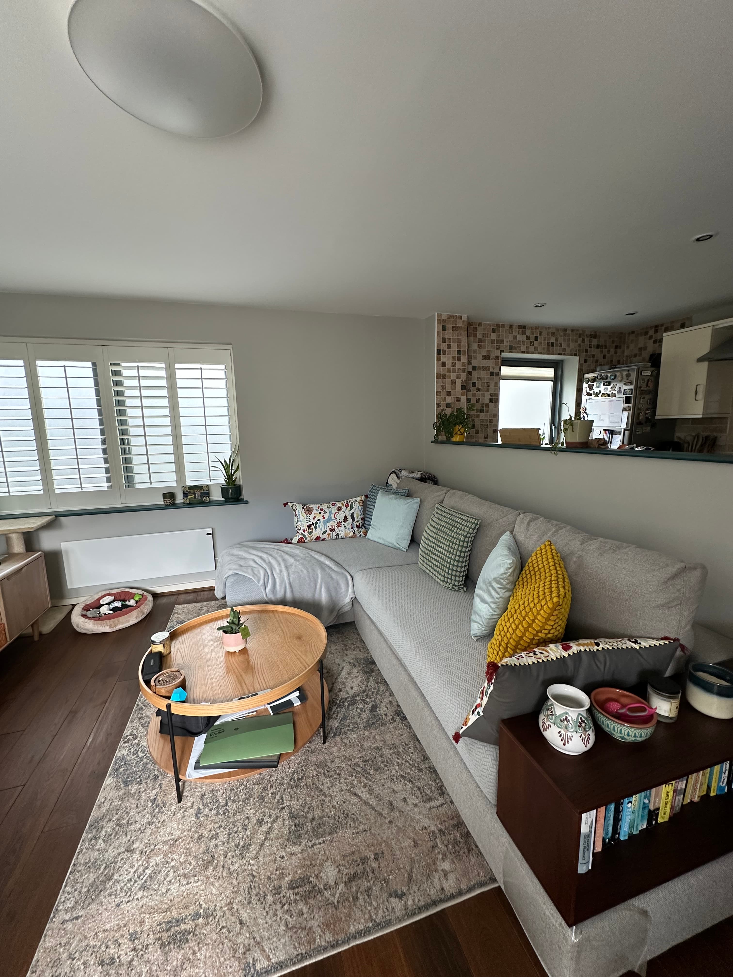 Grey sectional sofa with colorful pillows and a round wooden coffee table on a patterned rug.