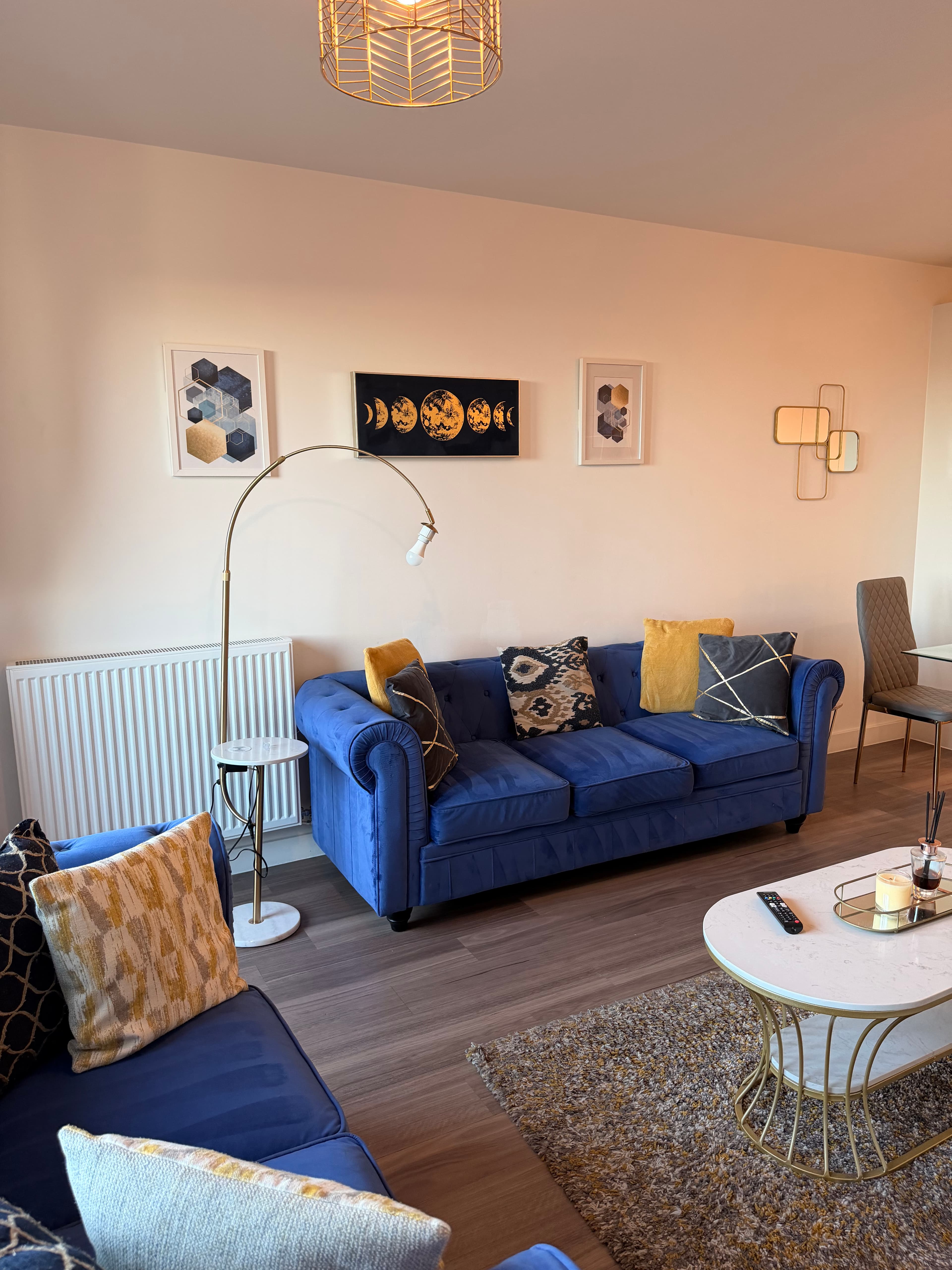 Modern living room with blue velvet sofa, gold floor lamp, and moon phase wall art.